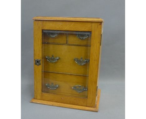 Small light oak cabinet with a glazed door, opening to reveal two short and two long drawers, 33cm high