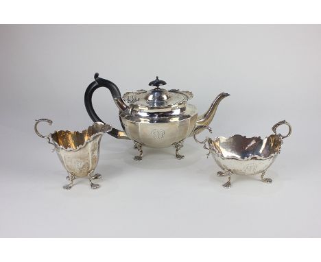 A George V silver three-piece tea set, oval faceted form with scroll borders, comprising teapot, two-handled sugar bowl and c