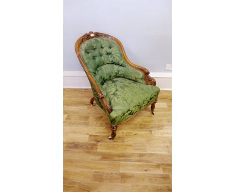A late Victorian carved mahogany framed button back lounge chair upholstered in a green floral fabric raised on turned suppor