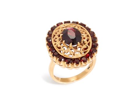 A garnet cluster ring, composed of a central oval mixed-cut garnet within openwork scroll surround and circular-mixed cut gar