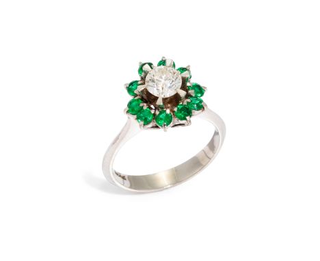 An emerald and diamond cluster ring, composed of a central round brilliant-cut diamond, in raised claw setting, with circular