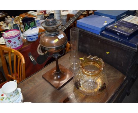 A copper oil lamp, raised on wooden base and floral decorated shade