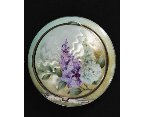 A silver and enamel ladies engine turned compact. The circular enamel set compact having silver banding with floral spray to 