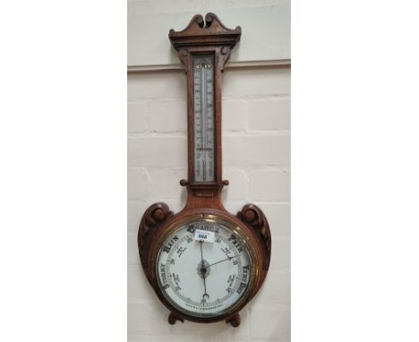 An Edwardian carved oak aneroid barometer and thermometer 