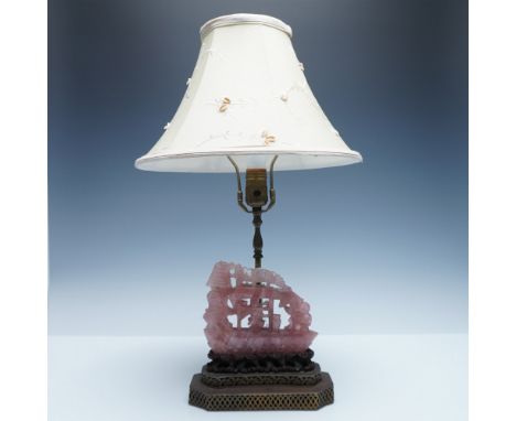 A unique table lamp featuring an intricately carved rose quartz ship mounted on a decorative wooden base. The lamp is topped 