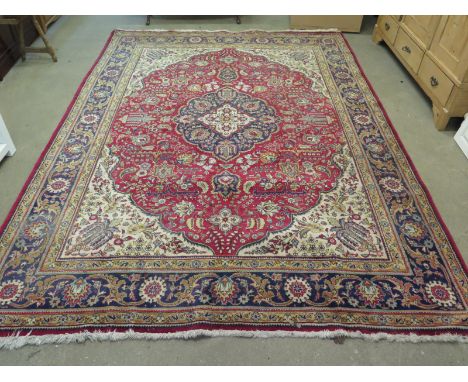 A large 20th century Eastern red ground hand knotted wool rug with floral and foliate designs and short fringe - 340cm x 240c