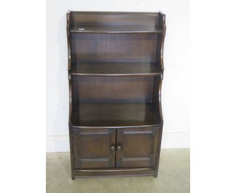 An Ercol waterfall bookcase with cupboard base - Height 111cm x Width 62cm x Depth 35cm