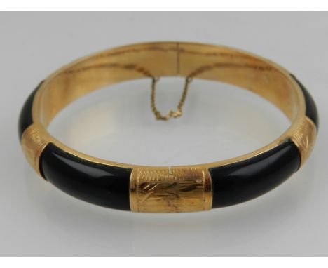 A 14 carat yellow gold and onyx circular bangle, having engraved decoration, safety chain, the clasps stamped 585. 