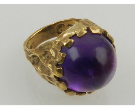 A 9 carat yellow gold and amethyst ring, set round cut cabouchon stone within a Modernist style mount. 