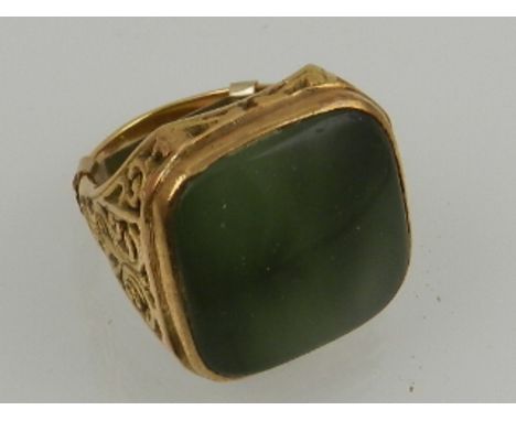 A yellow metal and green jade ring, set square cut jade within an ornately cast mount. 