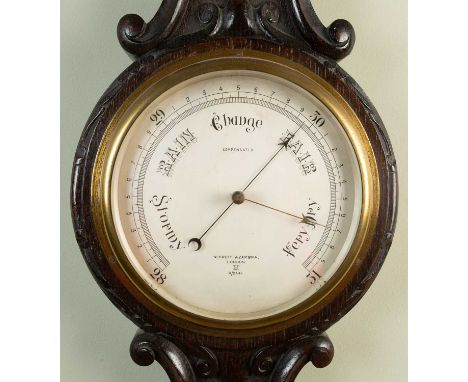 An oak cased aneroid thermometer and barometer by Negretti &amp; Zambra of London with carved scrolling ornament to the case,
