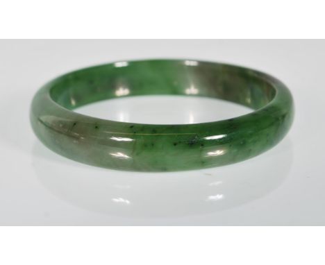 A Chinese green jade slave bangle of round plain form.
