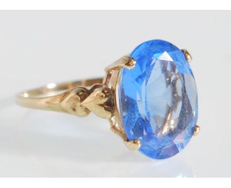 A hallmarked 9ct gold ladies dress ring prong set with an oval cut blue stone having heart decoration to the shoulders. Hallm