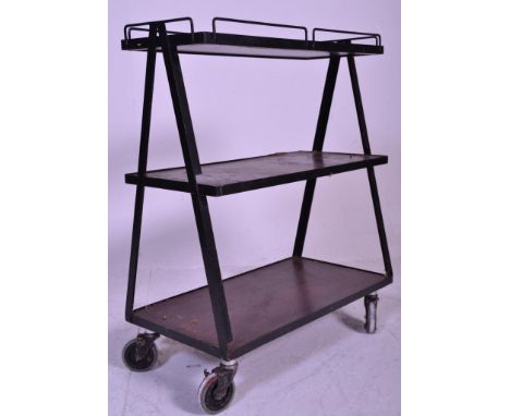 A retro mid century library trolley having black metal a-frames with castors supporting graduating 3 tiers with the top tray 