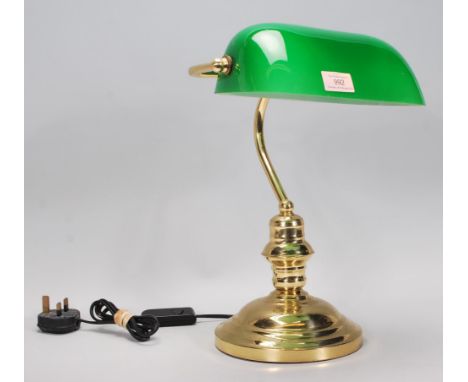 A vintage style bankers desk lamp having an adjustable green glass shade raised on a brass support and stepped brass base.