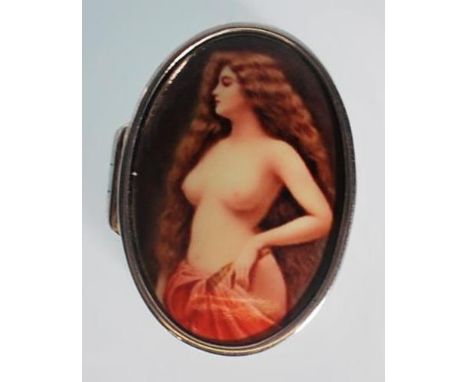 A small silver pill box in an oval shape featuring an enamelled lid. The enamel depicts a female nude who has hair to her wai