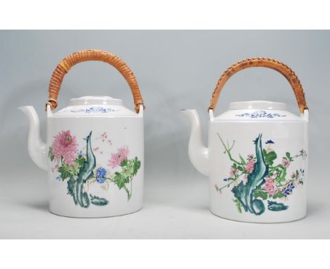 A pair of large Chinese polychrome teapots of cylindrical form having floral sprays to each with blue scroll motifs to the ne