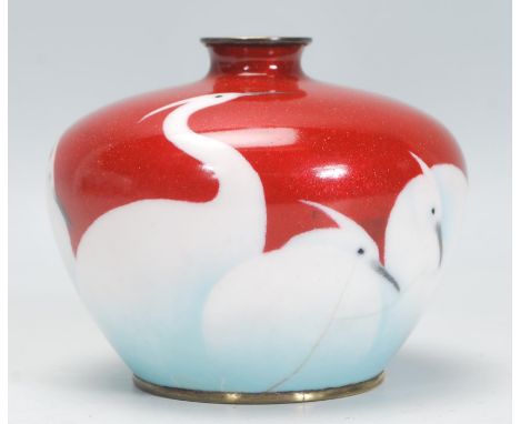 An early 20th Century Japanese cloisonne vase having red ground with multiple white cranes towards the base fading into a lig