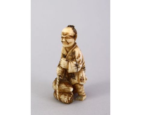 A SMALL JAPANESE MEIJI PERIOD CARVED IVORY NETSUKE - the figure carved holding tied sacks of straw, 5cm high.