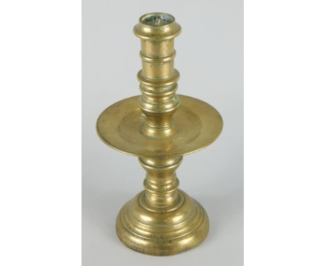 A late 17thC/early 18thC brass candlestick, with a barrel shaped sconce, a broad drip pan and a tapering base, possibly Dutch