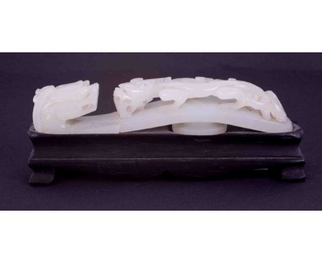 A Chinese carved white jade belt buckle, depicting a dragon on a dragon bridge, length 9cm on a black wood base, length 10cm 