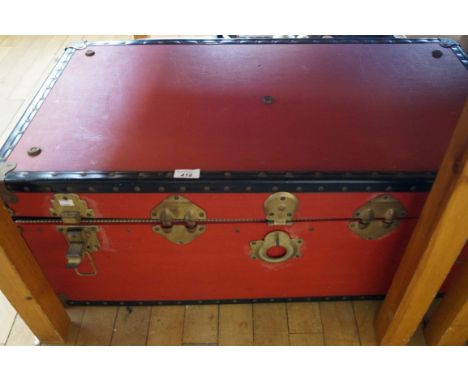 A vintage red trunk containing an assortment of sundry items.
