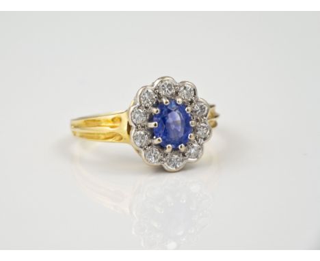 An 18ct gold, cornflower blue sapphire and diamond cluster ring, hallmarked London 1990, the oval cut sapphire within a borde