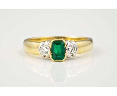 An 18ct yellow gold, emerald and diamond three stone ring, the central rub over set emerald flanked by a pair of brilliant cu