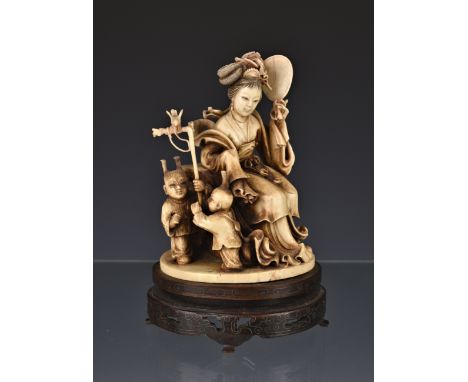 A Japanese carved ivory group of a noblewoman and two children, Meiji period (1868-1912), the woman seated open a rocky outcr