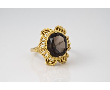 A 9ct yellow gold and smoky quartz ring, hallmarked London 1973, the oval cut smoky quartz claw set over a petalled filigree 