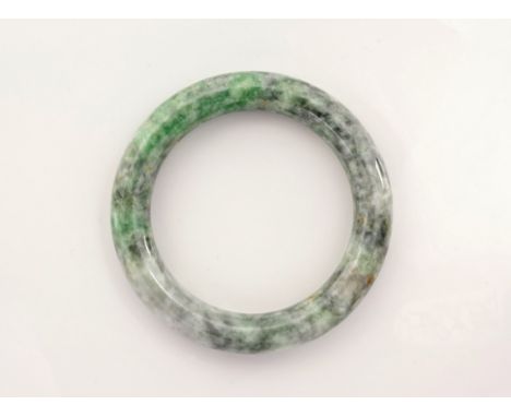 A carved jade bangle, believed to be Burmese, in mottled apple green, celadon and grey jade, 3¼in. (8.25cm.) diameter.