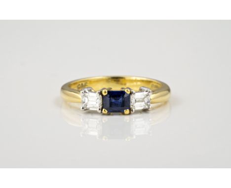 An 18ct gold, sapphire and diamond three stone ring, hallmarked London 1997, the central emerald cut sapphire flanked by a pa