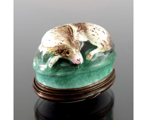 An 18th century Bilston enamel patch box, modelled in relief as a resting stag on grassy tuft, the lid painted with floral bo