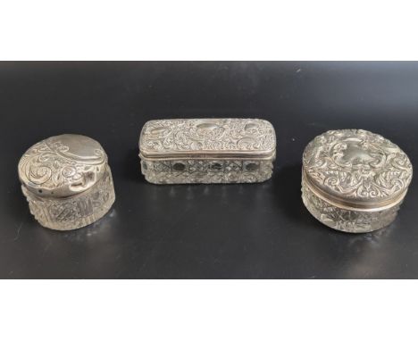 THREE EARLY 20th CENTURN SILVER TOPPED GLASS DRESSING TABLE POTSall with profuse scroll decoration to the embossed covers 