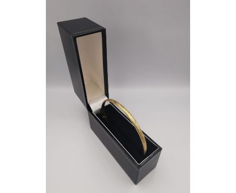 A boxed 9ct yellow gold textured and engraved bangle with a hidden pin clasp with safety catch. Hallmarked: 375, London. Weig