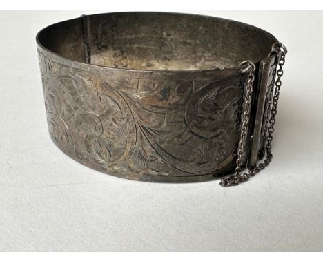 An Art Deco engraved wide silver bangle, decorated with scrolling foliate design. Fastens with a hidden hook clasp with slidi