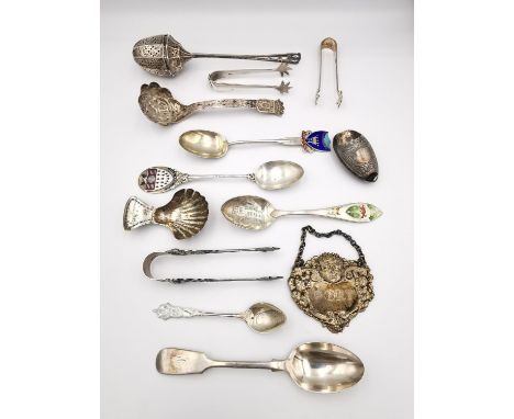 A collection of silver cutlery and other items, a silver repoussé drinks label, a tea strainer, three pairs of sugar tongs an