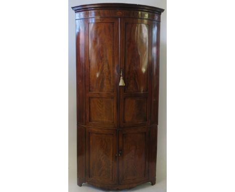 A large George III mahogany floor standing corner cupboardMoulded cornice over four panelled doors with lined inlaid decorati