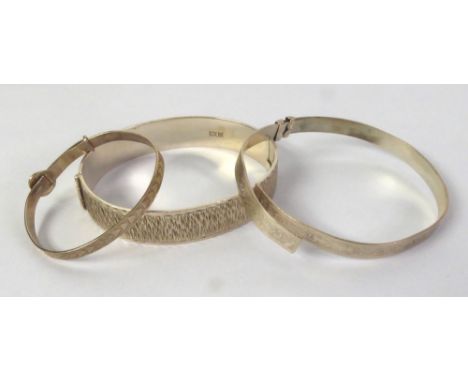 SILVER HINGE OPENING BROAD BANGLE  with textured top, CHILD'S BANGLE with chased decoration expanding through a buckle and AN