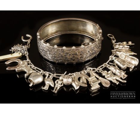 A late Victorian engraved silver bangle; and a silver charm bracelet with 25 various silver charms (2)