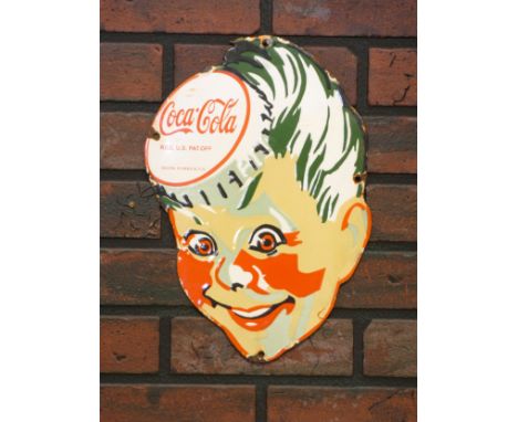 A vitreous enamel Coco-Cola sign, depicting a child's face with a bottle cap, 23cm x 34.5cm