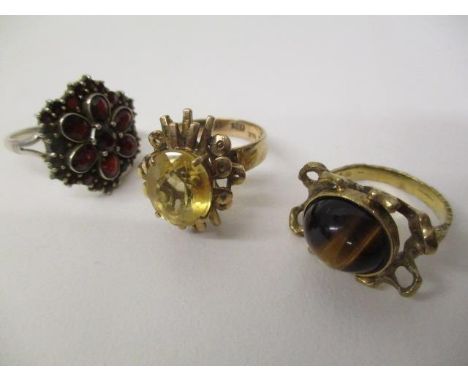 Two 9ct gold rings, one set with a tigers eye cabochon and the other a citreen, 10.1g and a white metal ring set with garnets