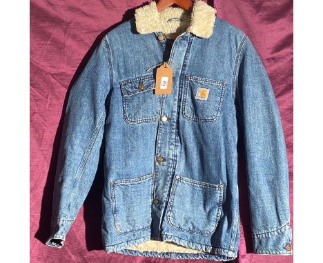 Carhartt sherpa-lined denim jacket with brass button closure, dual chest pockets, and internal pocket. Features signature log