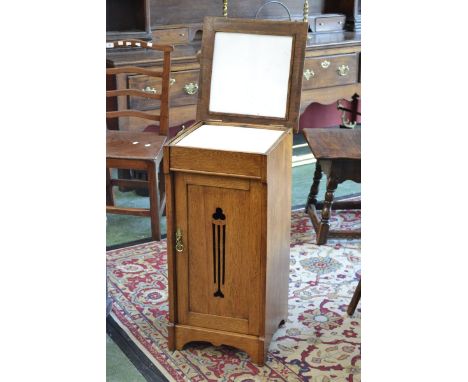 An Arts and Crafts oak wash stand, hinged moulded square top enclosing circular basin, pieced panel door, shaped apron.