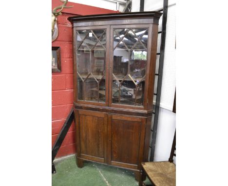 A George III oak and mahogany splay fronted floor standing corner cupboard, moulded outswept cornice and deep frieze above a 