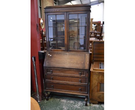 A 1940's oak bureau bookcase, two glazed doors enclosing shelving to top, fall front enclosing pigeonholes over three graduat