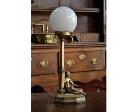 An Art Deco silvered figural table lamp, cast as a female nude seated beside a casket, opaque globular shade, lozenge shaped 