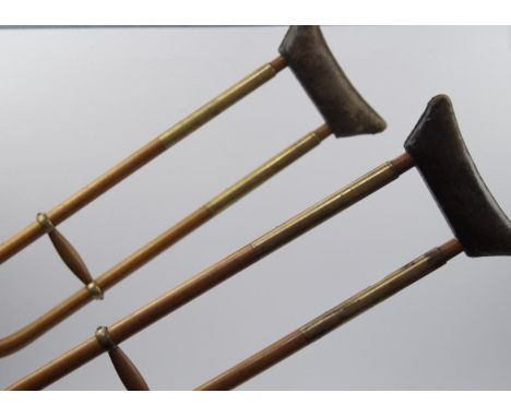 A pair of vintage wooden crutches, with brass mounts and leather pads.