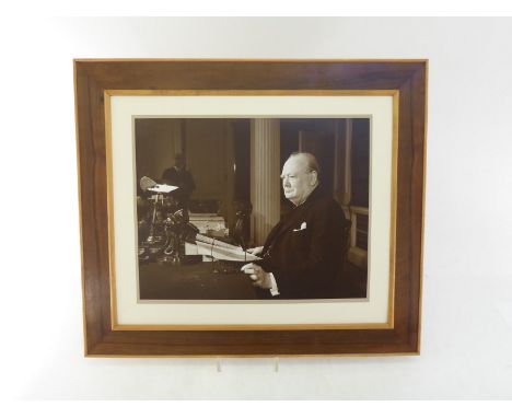A print of Sir Winston Churchill seated at his desk broadcasting to the nation. Mounted and framed in walnut and sycamore by 