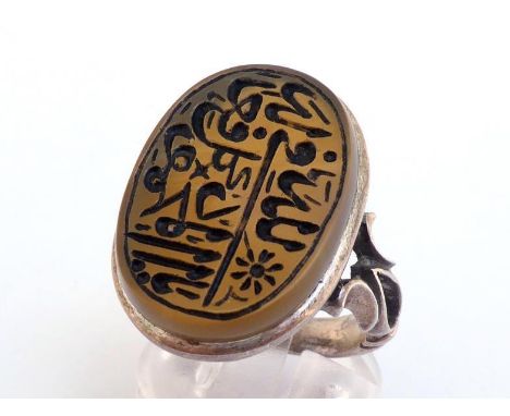 A Middle Eastern white metal (tests silver) and hardstone ring, the oval agate intaglio cut with Arabic text, 25 x 18mm wide,